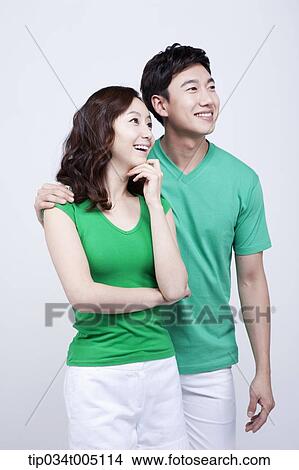 Picture - a man and a woman in green t-shirt smiling while looking at same place. Fotosearch
