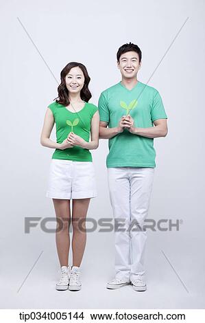 Picture - a man and a woman standing still holding sprouts with two hands . Fotosearch