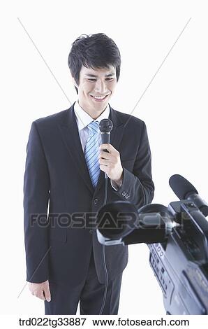 Stock Photo - a man in a black suit speaking with a microphone in front of a studio camera. Fotosearch