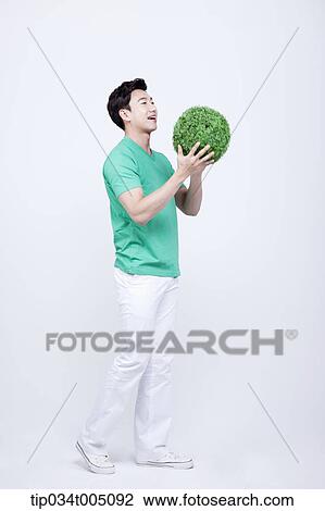 Stock Image - a man in green t-shirt holding a ball made from grass. Fotosearch