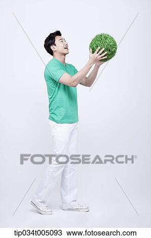 Stock Image - a man in green t-shirt holding a ball made from grass. Fotosearch