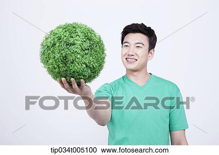 Stock Image - a man in green t-shirt holding a ball made from grass. Fotosearch