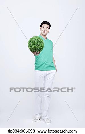 Stock Photo - a man in green t-shirt holding a ball made from grass. Fotosearch