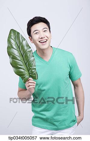 Stock Photo - a man in green t-shirt holding a huge leaf. Fotosearch
