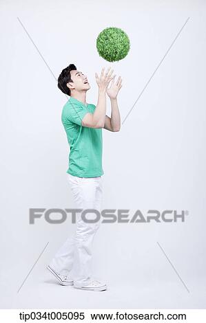 Stock Photography - a man in green t-shirt tossing a ball made from grass . Fotosearch