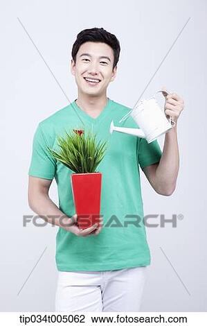 a man in green t-shirt watering a plant in a red vase View Large Photo Image Stock Image - a man in green t-shirt watering a plant in a red vase. Fotosearch