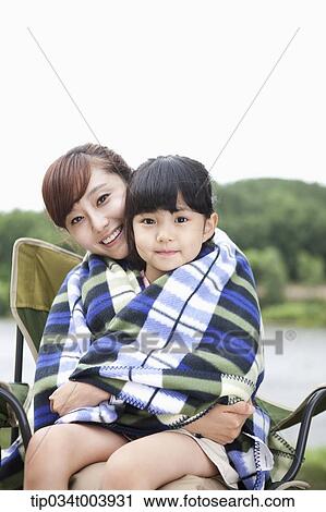 Stock Image - a mother and a daughter sitting on mother's lap having a blanket together. Fotosearch