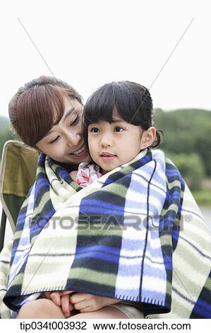 Stock Image - a mother and a daughter sitting on mother's lap having a blanket together. Fotosearch