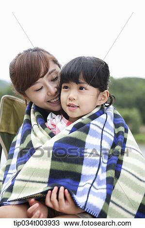 Stock Image - a mother and a daughter sitting on mother's lap having a blanket together. Fotosearch