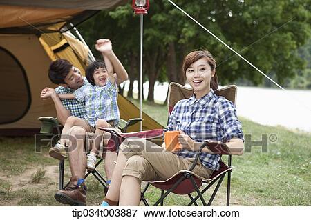 Stock Photo - a mother drinking a coffee while father plays with a son on a chair. Fotosearch