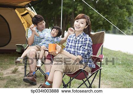 Stock Photo - a mother drinking a coffee while father plays with a son on a chair. Fotosearch