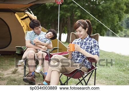 Stock Photo - a mother drinking a coffee while daughter sits on father's lap . Fotosearch