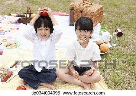 Stock Photography - a son holding a tomato on his head with a sister next to him . Fotosearch