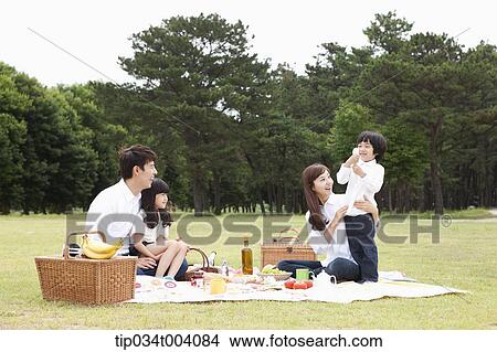 Picture - a son stood up in a picnic blanket while family having a picnic. Fotosearch