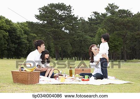 Stock Photograph - a son stood up in a picnic blanket while family having a picnic. Fotosearch
