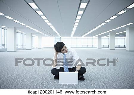 Stock Photograph - a stressed businessman using laptop on the floor of an empty room. Fotosearch