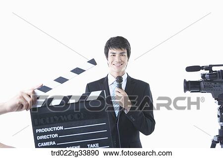 Stock Image - a studio camera and action board in front of man in a black suit with a microphone . Fotosearch