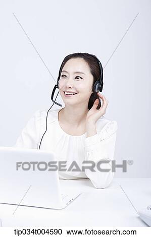 Stock Image - a telemarketer smiling touching her headset. Fotosearch