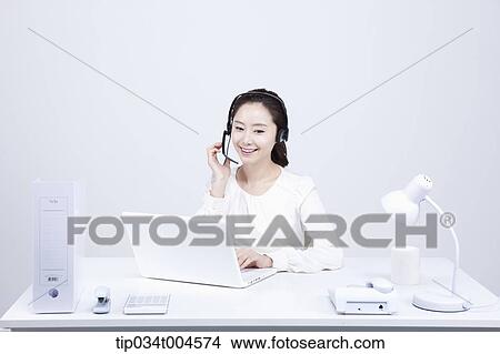 Picture - a telemarketer working at a white office desk. Fotosearch
