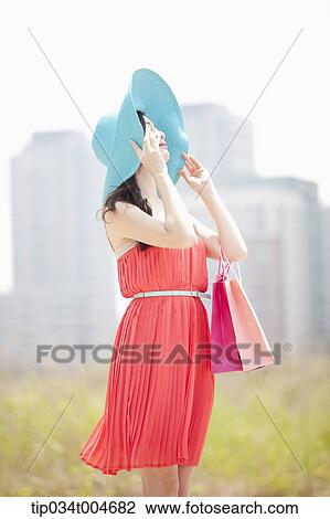 A woman covering her face with turquoise hat holding a shopping bags View Large Photo Image Stock Image - A woman covering her face with turquoise hat holding a shopping bags. Fotosearch