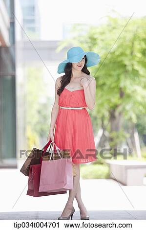A woman in a dress and hat walking with many shopping bags View Large Photo Image Stock Image - A woman in a dress and hat walking with many shopping bags. Fotosearch