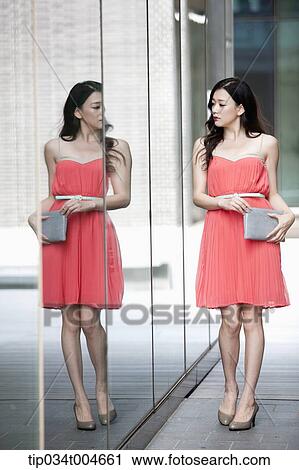 A woman in coral dress and grey clutch walking along a glass wall View Large Photo Image Stock Image - A woman in coral dress and grey clutch walking along a glass wall. Fotosearch