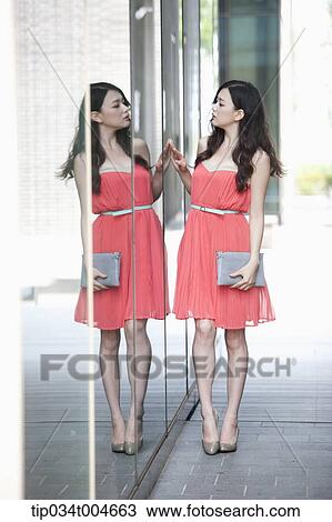 A woman in coral dress and grey clutch looking herself through a glass wall View Large Photo Image Stock Image - A woman in coral dress and grey clutch looking herself through a glass wall. Fotosearch