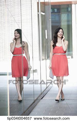 A woman in coral dress and grey clutch walking along a glass wall View Large Photo Image Stock Photo - A woman in coral dress and grey clutch walking along a glass wall. Fotosearch