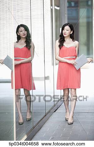 A woman in coral dress and grey clutch walking along a glass wall View Large Photo Image Stock Photo - A woman in coral dress and grey clutch walking along a glass wall. Fotosearch