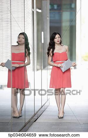 A woman in coral dress and grey clutch walking along a glass wall View Large Photo Image Stock Photo - A woman in coral dress and grey clutch walking along a glass wall. Fotosearch
