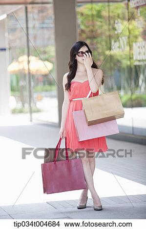 A woman in coral dress and sunglasses holding many shopping bags View Large Photo Image Picture - A woman in coral dress and sunglasses holding many shopping bags. Fotosearch