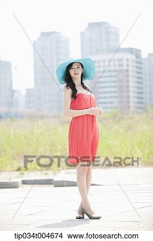 A woman in coral dress and turquoise hat posing in front of grass field View Large Photo Image Picture - A woman in coral dress and turquoise hat posing in front of grass field. Fotosearch