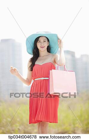 A woman in coral dress and turquoise hat holding a shopping bag View Large Photo Image Stock Photo - A woman in coral dress and turquoise hat holding a shopping bag . Fotosearch
