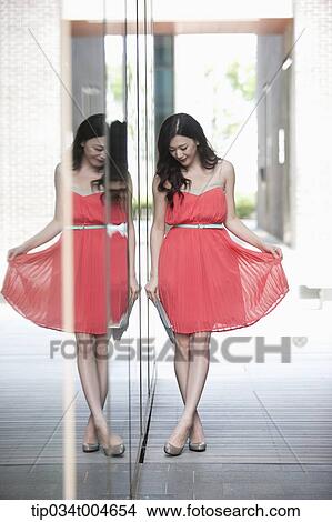 Picture - A woman in coral dress lifting up her dress. Fotosearch
