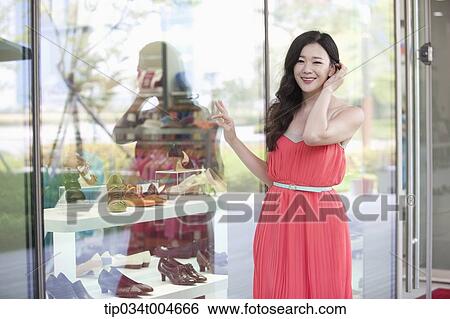 Stock Photograph - A woman in coral dress pointing something on a show window. Fotosearch