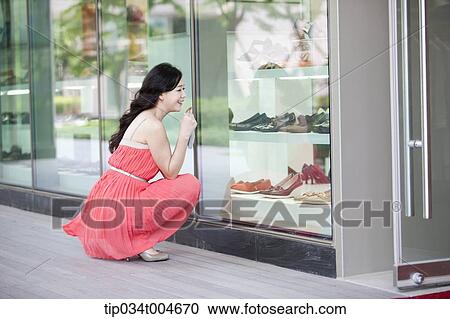 Stock Image - A woman in coral dress sitting in front of show window in crouched position. Fotosearch
