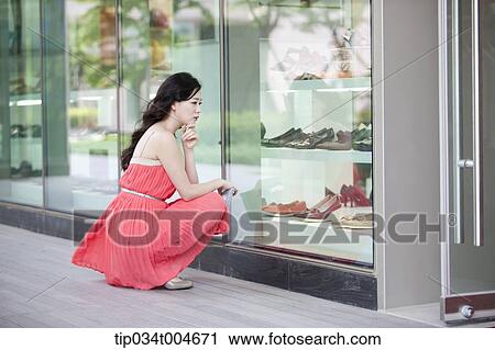 Stock Image - A woman in coral dress sitting in front of show window in crouched position. Fotosearch
