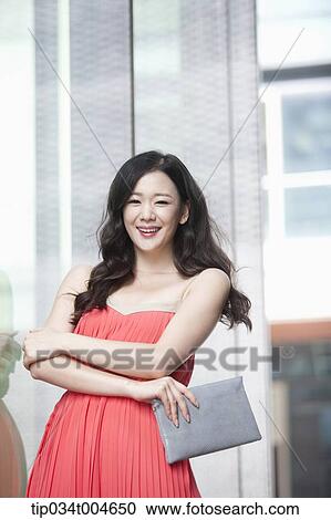 Stock Image - A woman in coral dress smiling next to a glass wall. Fotosearch