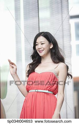 Stock Image - A woman in coral dress smiling next to a glass wall. Fotosearch