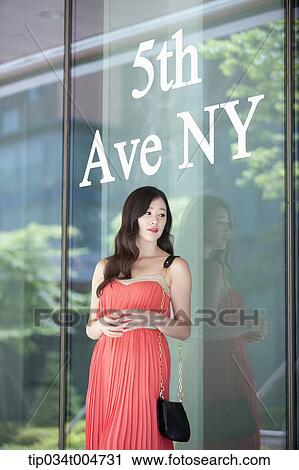 Stock Image - a woman in coral dress standing in front of a show window with a 8th Ave NY sign. Fotosearch