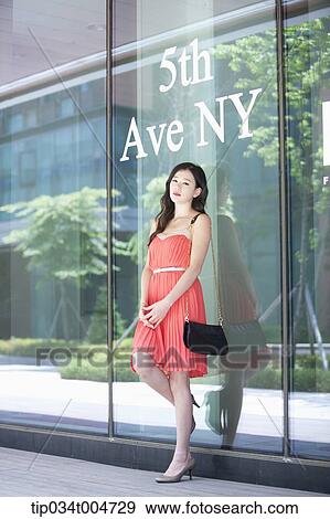 Stock Photo - a woman in coral dress standing in front of a show window with a 6th Ave NY sign. Fotosearch