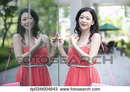 Stock Image - A woman in coral dress standing next to a glass wall. Fotosearch