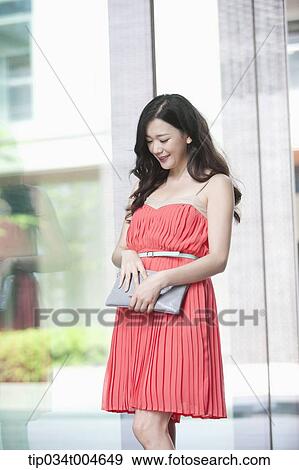 A woman in coral dress touching her clutch View Large Photo Image Stock Photo - A woman in coral dress touching her clutch. Fotosearch