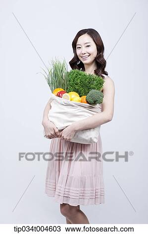 Stock Image - A woman in dress holding a bag of vegetables. Fotosearch
