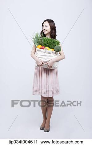 A woman in dress holding a bag of vegetables View Large Photo Image Stock Image - A woman in dress holding a bag of vegetables. Fotosearch