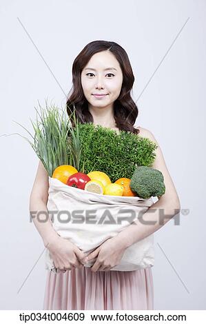 Stock Photo - A woman in dress holding a bag of vegetables. Fotosearch