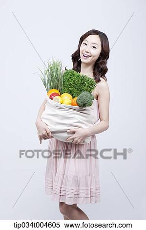 Stock Photography - A woman in dress laughing while holding a bag of vegetables. Fotosearch