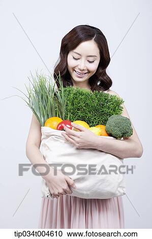 Stock Image - A woman in dress looking at a bag of vegetables in her arms. Fotosearch