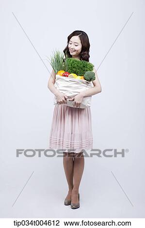 Stock Image - A woman in dress looking at a bag of vegetables in her arms. Fotosearch