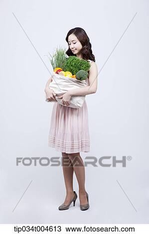 A woman in dress looking at a bag of vegetables in her arms View Large Photo Image Stock Image - A woman in dress looking at a bag of vegetables in her arms. Fotosearch